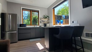 Ett modernt kök med kylskåp, mikrovågsugn och diskho. Det finns ett fönster med utsikt över träd och en stol placerad nära fönstret.