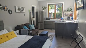 Ett kompakt bostadsutrymme med en säng, en soffa, ett litet kök och en matplats.