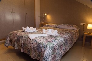 Una cama bien hecha con ropa de cama floral, una lámpara de noche y una lámpara fijada a la pared.