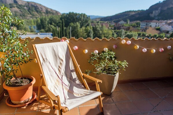 Un balcón con una silla de madera, una planta en maceta y vistas de un paisaje montañoso.