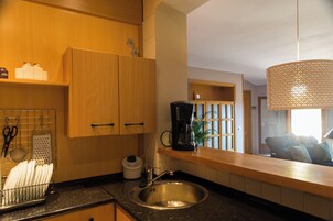 Una cocina con armarios de madera, un lavamanos de acero inoxidable, una cafetera y una lámpara colgante.