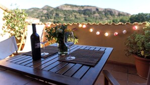 A wooden table with a bottle of wine and two glasses on a terrace with a view of hills. - La Terrasseta. Ático con terraza. (Graus)