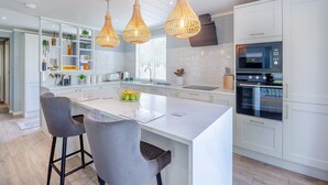A modern kitchen with white cabinetry, a central island, pendant lighting, and stainless steel appliances. - 2 bedroom accommodation in Benllech (Benllech)