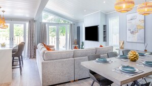 A modern living room with a sofa, dining table, and a TV mounted on the wall. - 2 bedroom accommodation in Benllech (Benllech)