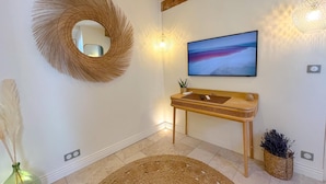 A modern bathroom with a wooden vanity, a large mirror, a wall-mounted TV, and a decorative woven rug. - 1 Bedroom Apartment in L'Isle-sur-la-Sorgue (L'Isle-sur-la-Sorgue)