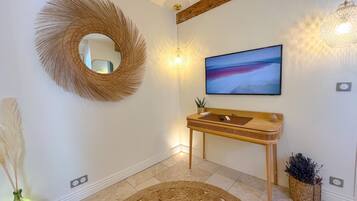 Une salle de bain moderne avec un meuble-lavabo en bois, un grand miroir, un téléviseur fixé au mur et un tapis décoratif tissé.