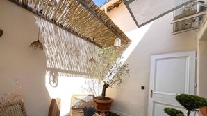 A small patio area with a yellow table, wicker chairs, a potted tree, and a white door. - 1 Bedroom Apartment in L'Isle-sur-la-Sorgue (L'Isle-sur-la-Sorgue)