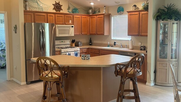 A modern kitchen with wooden cabinets, stainless steel appliances, and a central island with two bar stools. -  Sunsets on the Sands in the Villages! Golf Front  3/2 (The Villages)