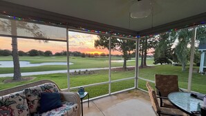 A covered patio with a view of a golf course at sunset, a wicker sofa, a table, and chairs. -  Sunsets on the Sands in the Villages! Golf Front  3/2 (The Villages)