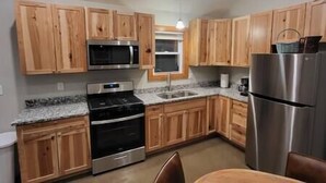 A kitchen with wooden cabinets, a stainless steel refrigerator, a microwave, an oven, and a sink. - Brightstone Lake Cabin 4 (Rensselaer)