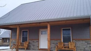 A building with a metal roof, wooden porch, and two windows. - Brightstone Lake Cabin 4 (Rensselaer)