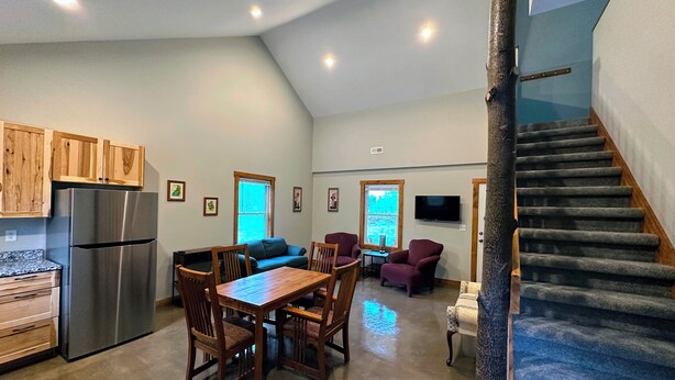 A spacious kitchen with wooden cabinets, a stainless steel refrigerator, and a dining area with a wooden table and chairs. - Brightstone Lake Cabin 4 (Rensselaer)