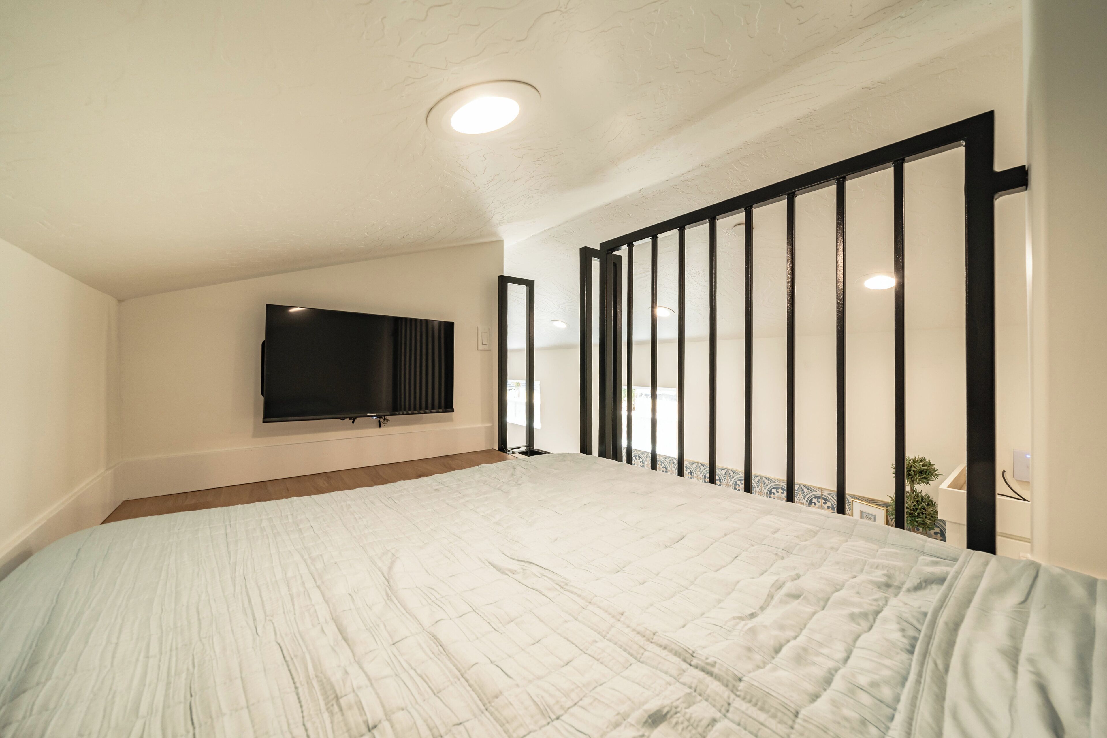 A bedroom with a large bed, a flat-screen TV mounted on the wall, and a balcony with a railing.