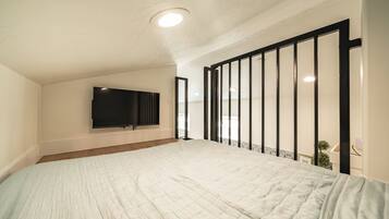A bedroom with a large bed, a flat-screen TV mounted on the wall, and a balcony with a railing.