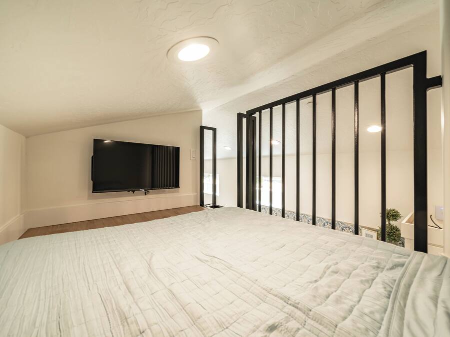 A bedroom with a large bed, a flat-screen TV mounted on the wall, and a balcony with a railing.