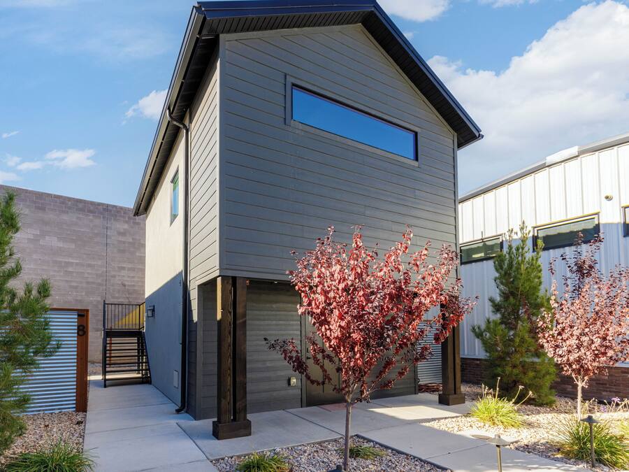 A modern two-story building with a garage door and a small tree in the front yard.
