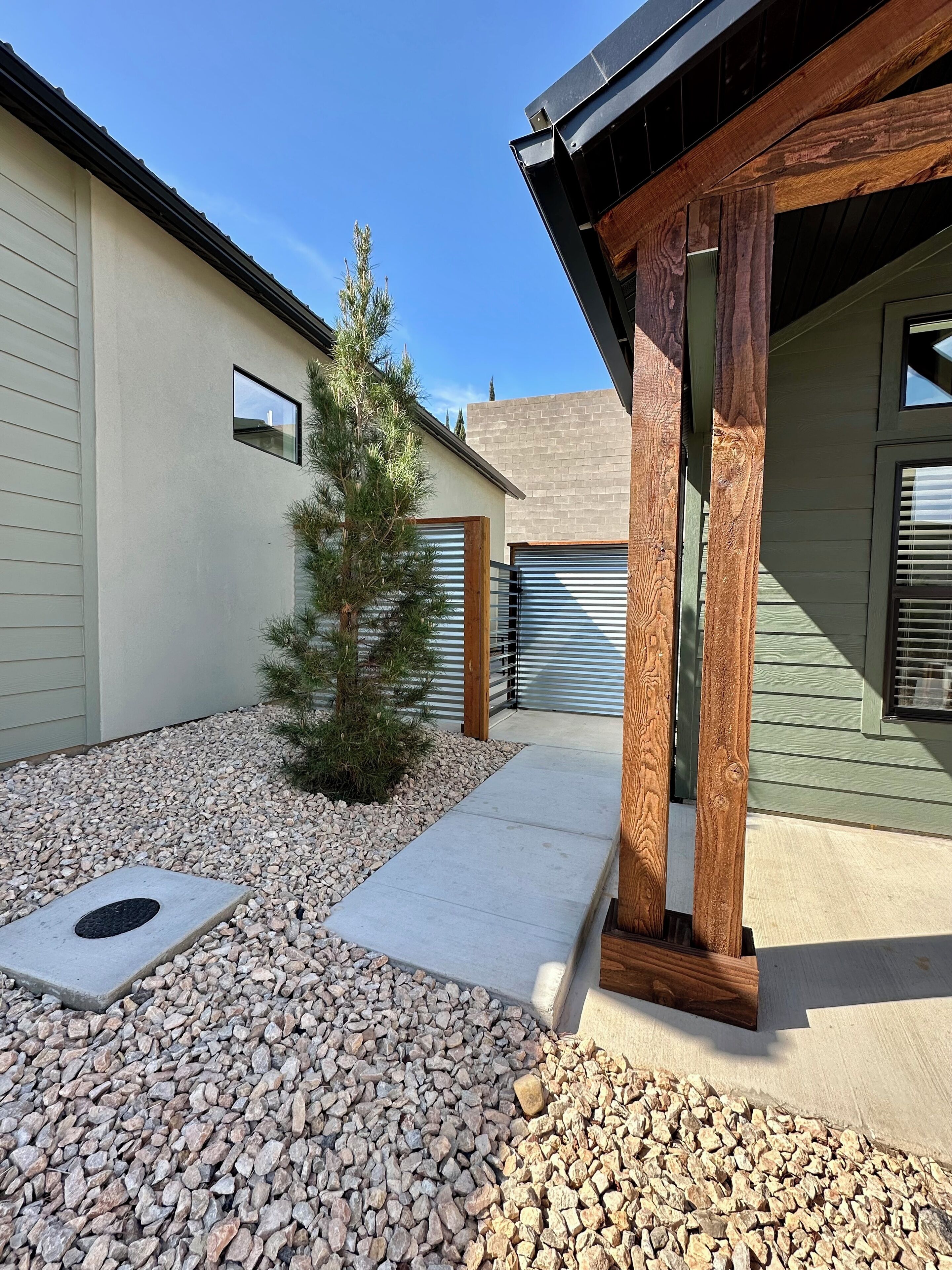 A residential property with a gravel driveway, a small pine tree, and a wooden pergola structure.