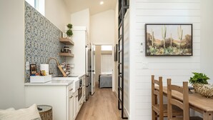 A modern kitchen with white cabinetry, a wooden dining table, and a cactus painting on the wall. - Zion Oasis Rentals (Hurricane)