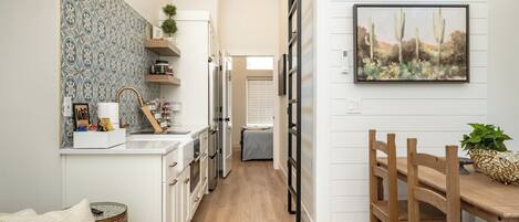 A modern kitchen with white cabinetry, a wooden dining table, and a cactus painting on the wall.