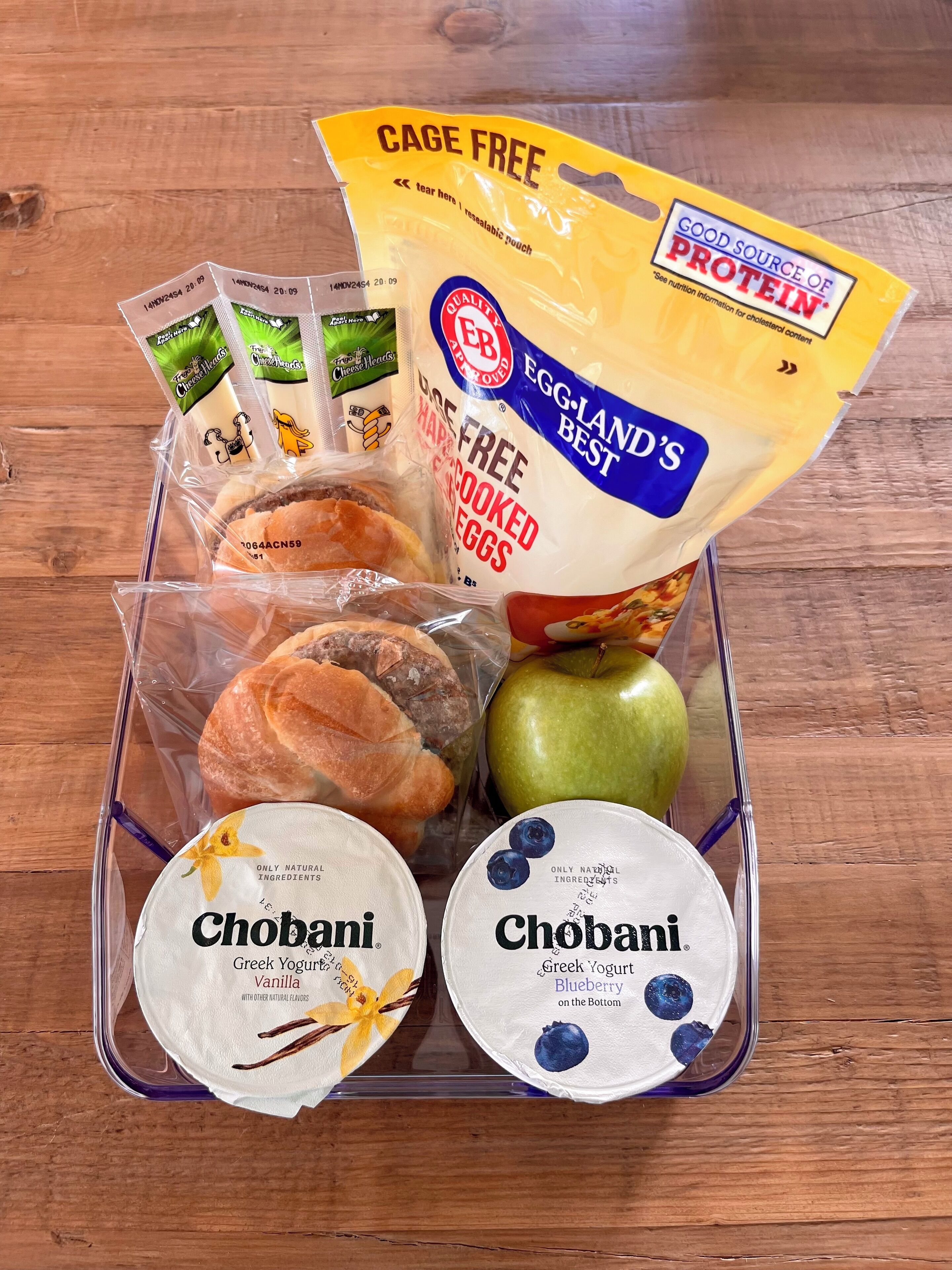 A meal prep with various food items including eggs, bread, an apple, and two containers of Chobani yogurt.