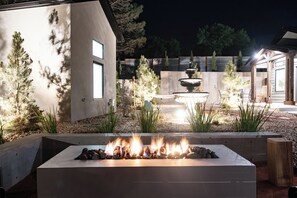 A modern outdoor patio with a fire feature, a stone planter, and a wooden pergola. - Zion Oasis Rentals  (Hurricane)