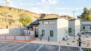 A modern building with a parking lot, a small garden area, and a mountainous backdrop. - Zion Oasis Rentals (Hurricane)