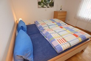 Un letto con un materasso blu e una coperta colorata, un comodino in legno con una pianta e un quadro appeso al muro.