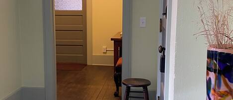 A hallway with wooden flooring, a glass table with a vase, and a door leading to another room.