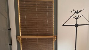 Una habitación con un gran ventanal con persianas, un atril y baldosas estampadas en el suelo.