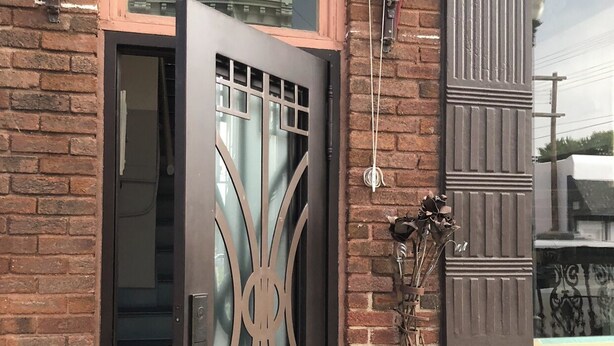Una puerta metálica marrón con un diseño decorativo, un muro de ladrillo y una ventana encima.