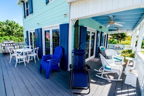 A covered outdoor deck with white wicker furniture, a blue lounge chair, and a grill area. - Ocean View, Sleeps 8, SUP, Beach Toys (Spanish Wells)