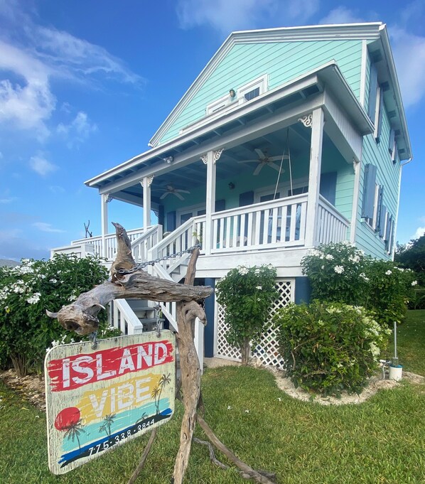 A turquoise house with a porch, surrounded by greenery and a 'VIBE' sign. - Ocean View, Sleeps 8, SUP, Beach Toys (Spanish Wells)