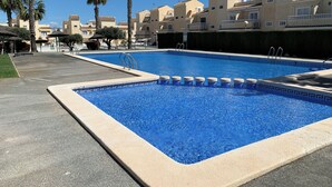 En swimmingpool med kristallklart blått vatten, omgiven av palmer och byggnader med tak belagda med tegelpannor.