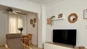 Ett vardagsrum med en TV, ett matbord, stolar, en soffa, en takfläkt och dekorativa föremål på väggarna.