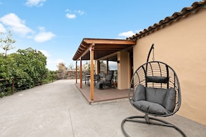 A covered patio area with a hanging chair, outdoor furniture, and a view of the surrounding landscape.
