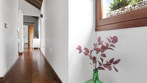 Ein Flur mit Holzboden, einer grünen Vase mit Pflanze und einem Fenster mit Blick auf Felsen und Grün.