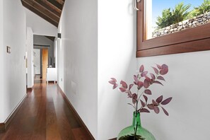 Un couloir doté d’un plancher en bois, d’un vase vert contenant une plante et d’une fenêtre donnant sur des rochers et de la verdure.