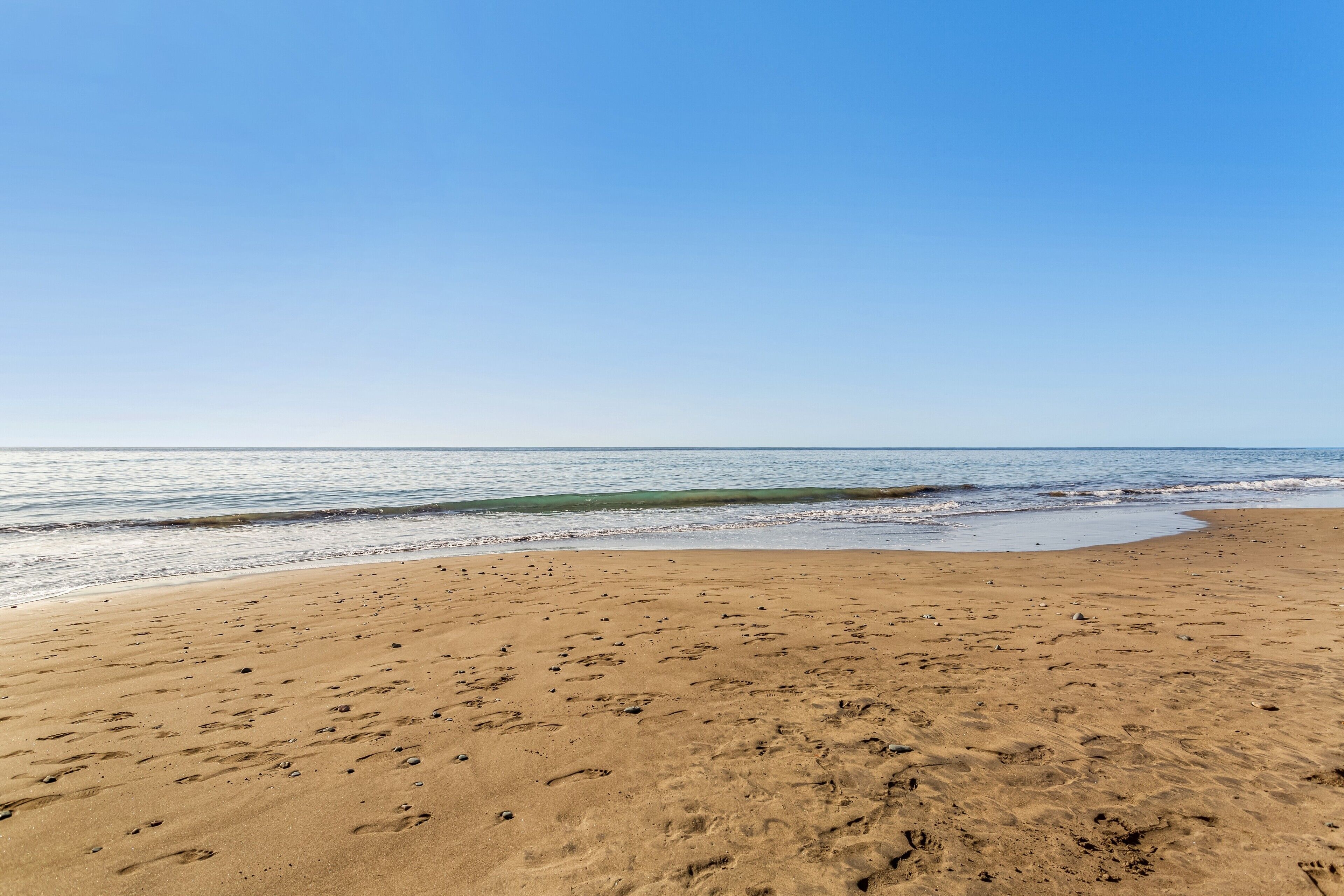 Una playa arenosa con huellas y un cielo azul despejado.