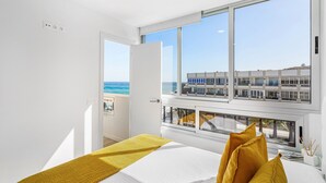 Ett modernt hotellrum med ett stort fönster, en säng med ett gult överkast och utsikt över en byggnad på andra sidan vattnet.