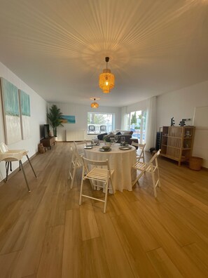 A spacious dining area with a round table, white chairs, and a ceiling light fixture.