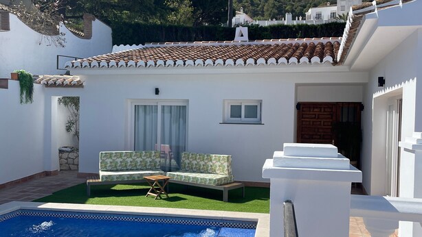Una piscina con balaustrada blanca, un patio con sofá y mesa, y montañas al fondo.