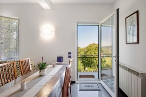 A modern interior with a dining area, a potted plant, a framed picture, and a balcony with a view. - Apartment 'Ai Campi' with Private Garden, Balcony, and Wi-Fi (Stella San Bernardo)