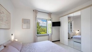Une chambre avec un grand lit, une fenêtre avec des rideaux, un téléviseur fixé au mur et une armoire avec un miroir.