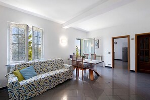 Una sala de estar moderna con sofá, mesa de comedor, sillas y un ventanal con persianas.