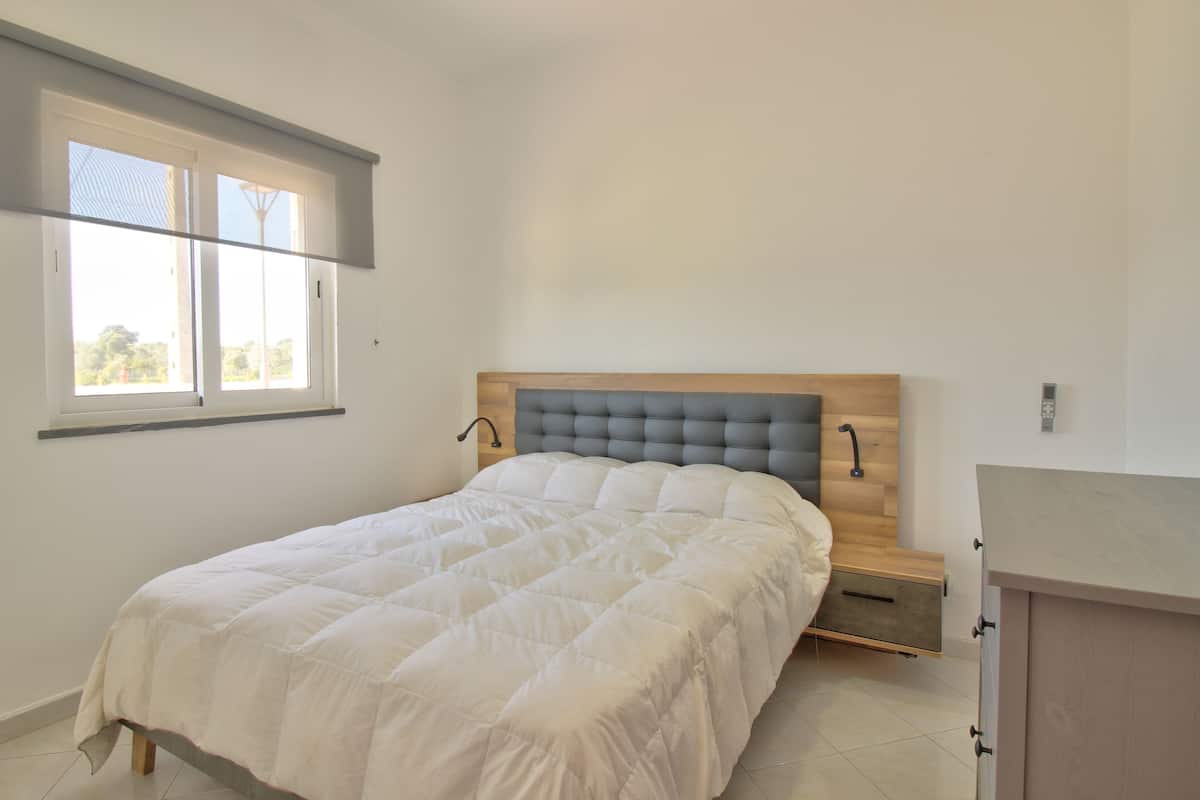Un dormitorio con cama, mesita de noche, cabecera de madera, ventana y armario empotrado.