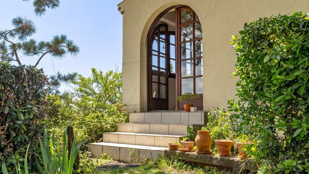 A building with a large arched window, steps leading to a door, and potted plants. - Bois Flottés Holiday Home – House with Garden, 700 Meters from the Sea (Pornic)