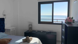 A bedroom with a bed, a nightstand, a dresser, a window with a view of the sea, and a lamp. - Apartment 'Apartamento Frontal Primera Linea' with Sea View, Wi-Fi and Air Conditioning (Fuengirola)