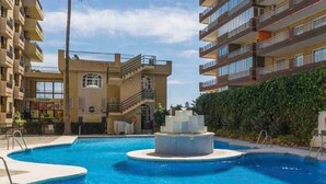 A swimming pool surrounded by multi-story buildings with balconies, palm trees, and a clear sky. - Apartment 'Apartamento Frontal Primera Linea' with Sea View, Wi-Fi and Air Conditioning (Fuengirola)