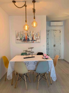 A dining area with a table set for four, a painting of sailboats on the wall, and a white door with a vintage design. - Apartment 'Apartamento Frontal Primera Linea' with Sea View, Wi-Fi and Air Conditioning (Fuengirola)