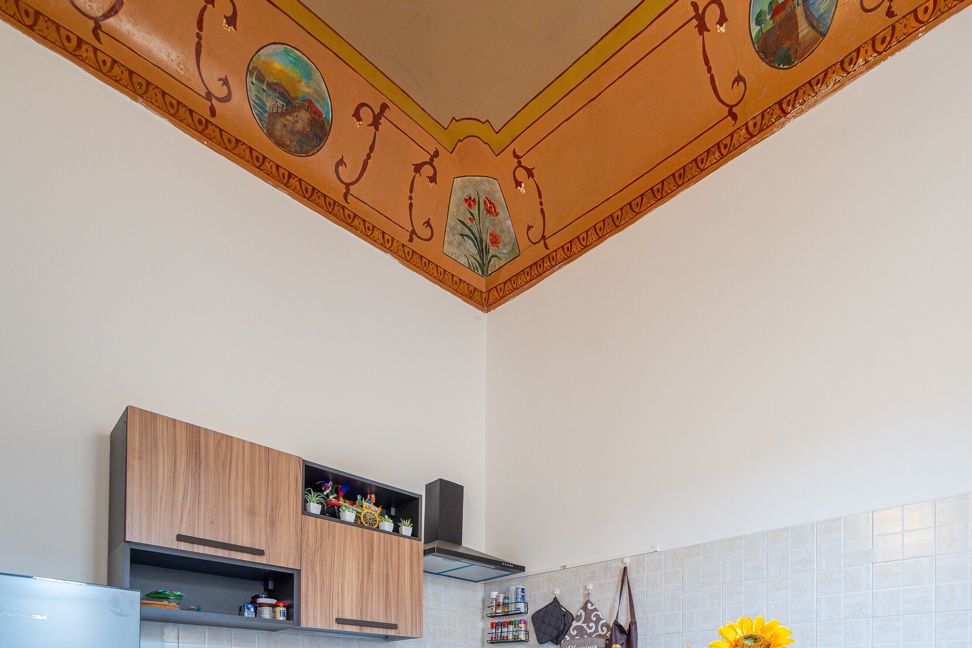 Une cuisine avec des meubles de rangement en bois, une cuisinière encastrée et un plafond décoratif orné de motifs floraux.
